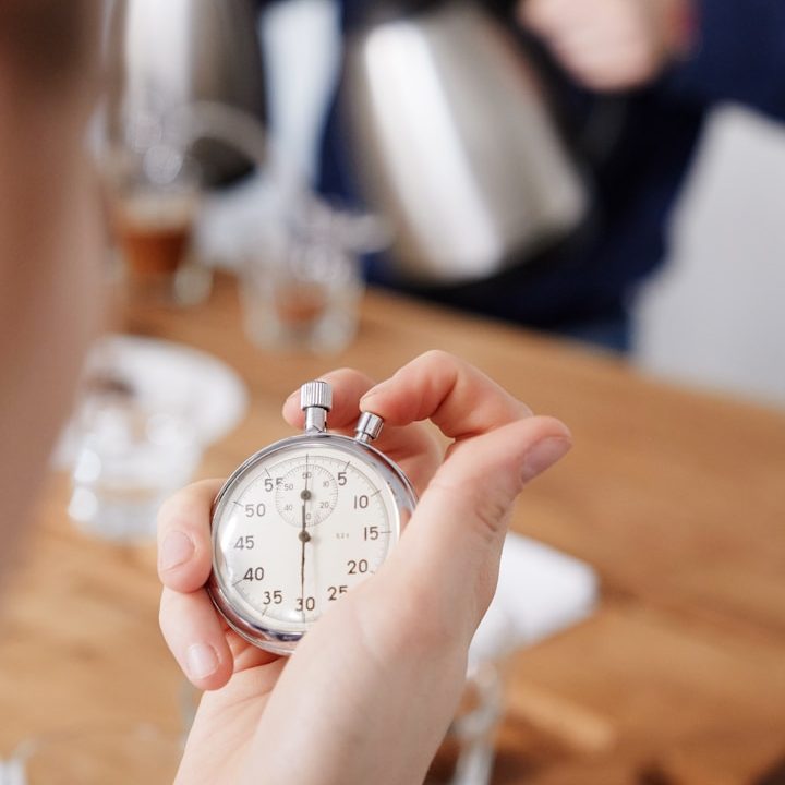 Eine Hand hält eine Stoppuhr über einem Holztisch mit Getränken.