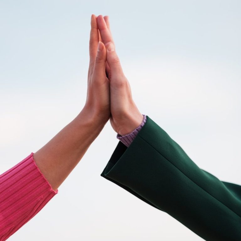 Zwei Hände berühren sich in einer hochgestreckten Höhe, eine pinke und eine grüne.