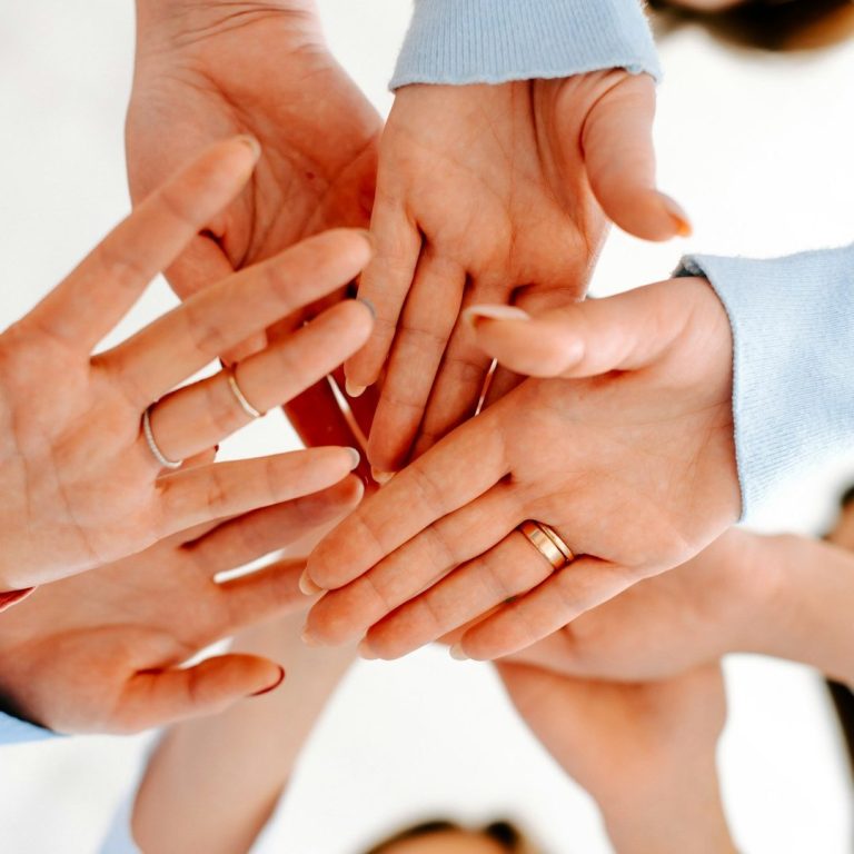Verschiedene Hände, die übereinander gelegt sind, symbolisieren Zusammenarbeit und Gemeinschaft.